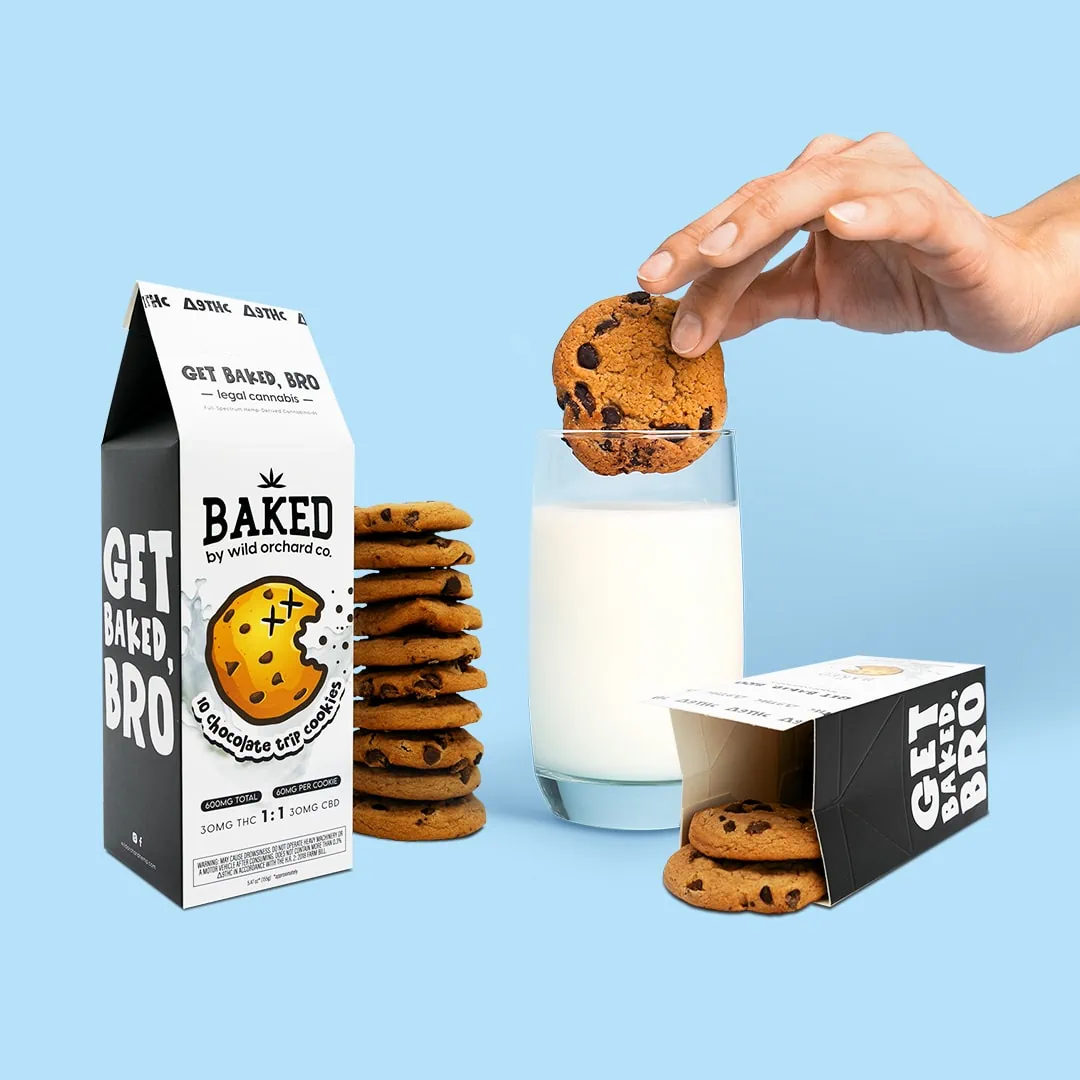 A person is holding a box of Baked Delta-9 Chocolate Trip Cookies and a glass of milk.