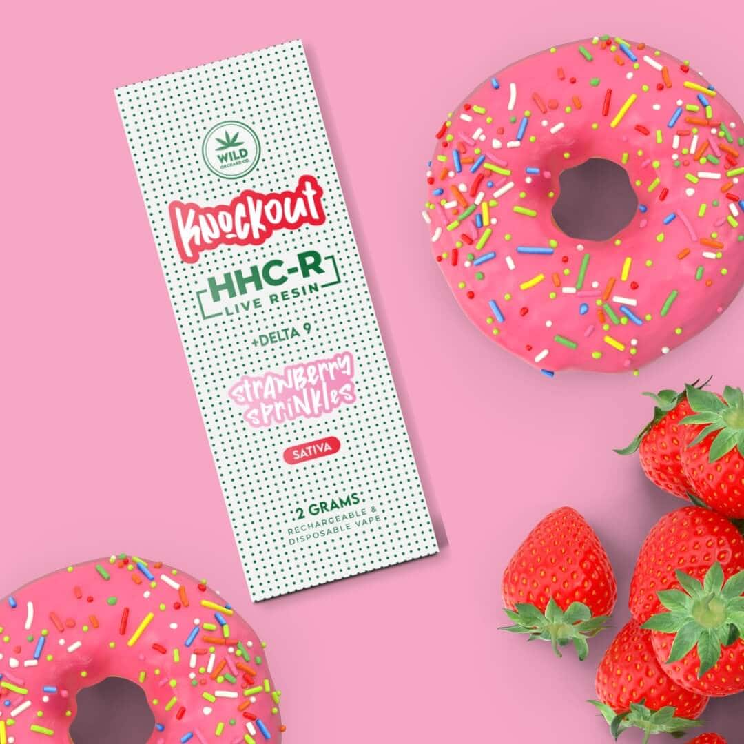 Donuts and a bottle of Knockout “Strawberry Sprinkles” HHC-R Live Resin Vape 2 Gram on a pink background.