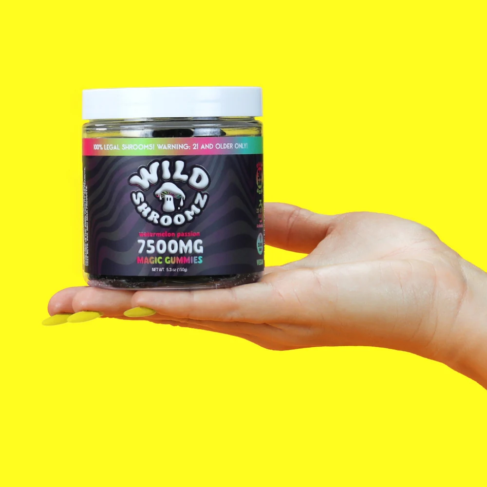 A hand holding a jar of Wild Shroomz Mushroom + Delta 9 Gummies "Watermelon Passion" against a bright yellow background.