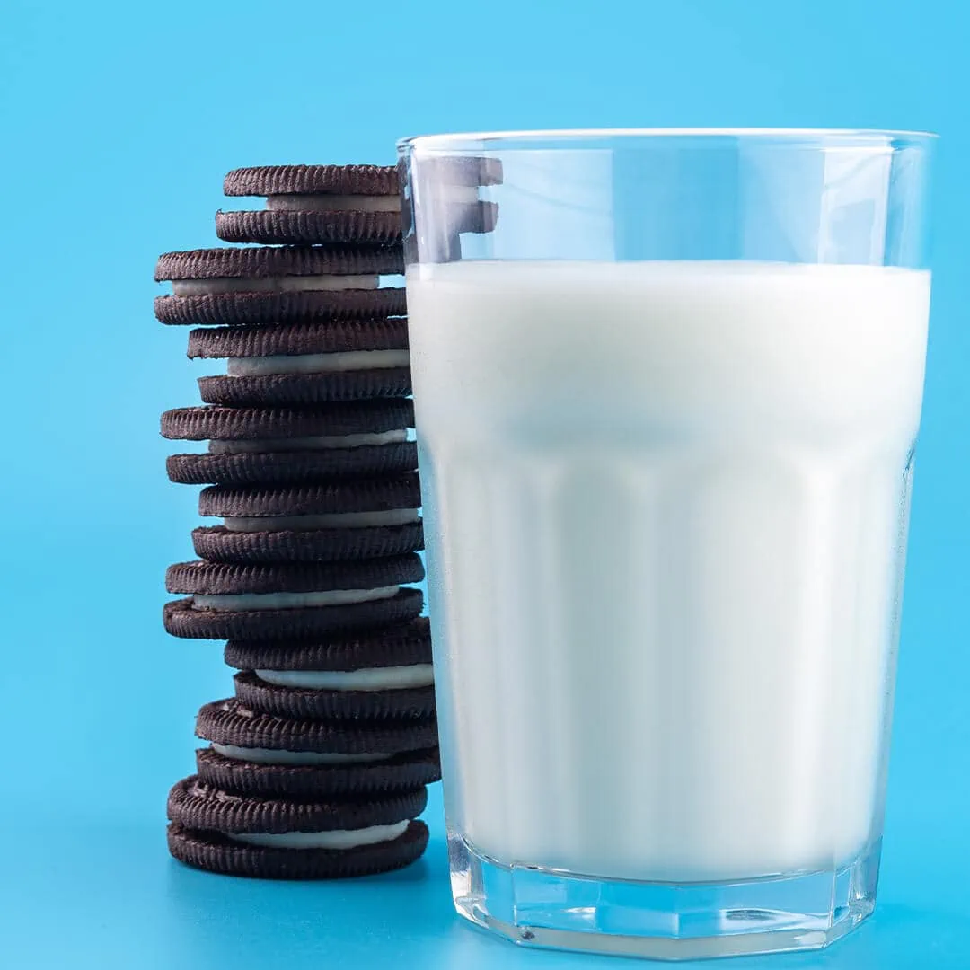 A glass of milk next to a stack of oreo cookies and a Baked Delta-9 Magic Brownie.