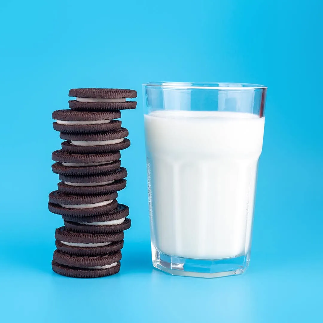 Oreo cookies and a glass of milk on a blue background with a Delta-9 Magic Brownie.