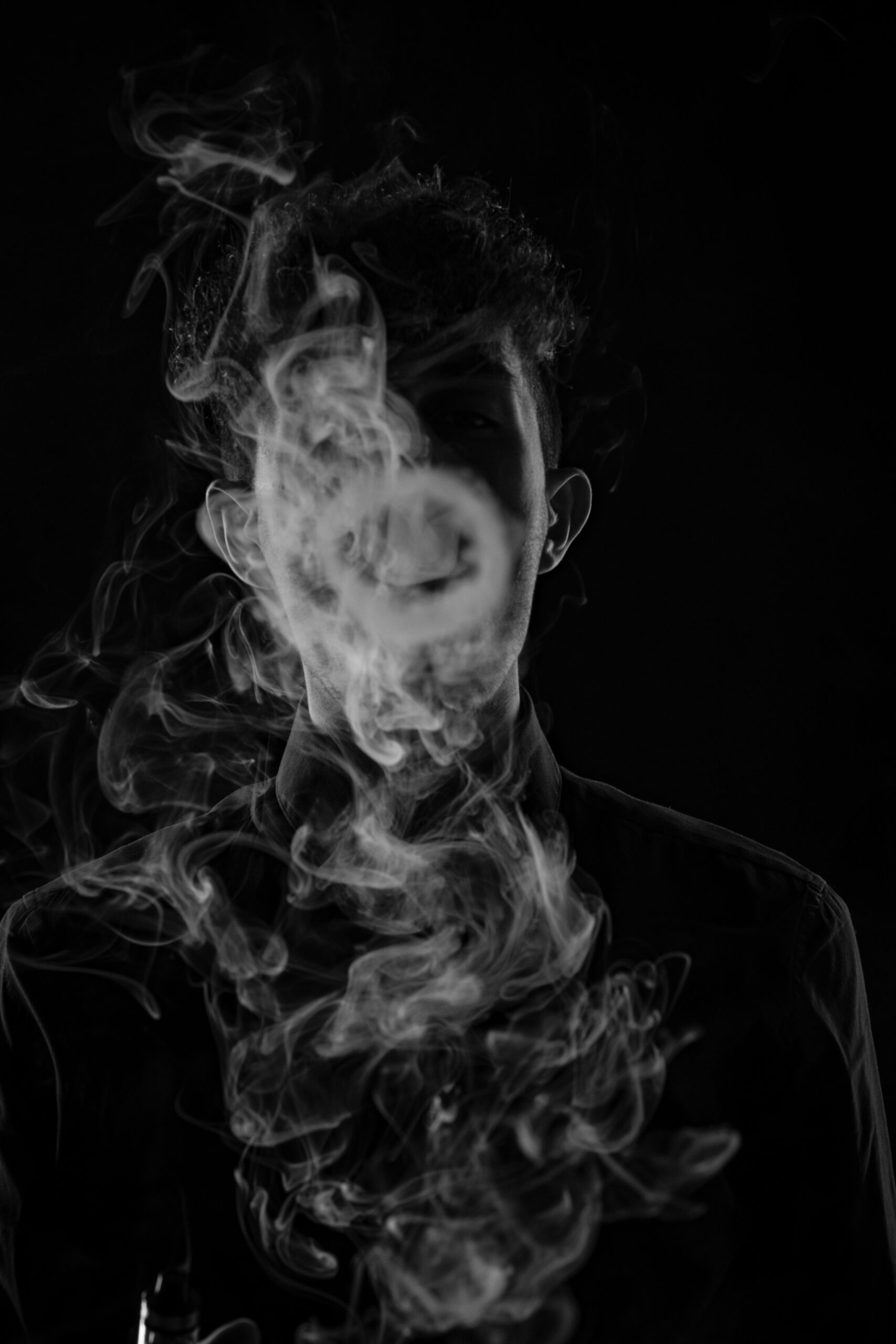 A person obscured by swirls of smoke against a dark background.