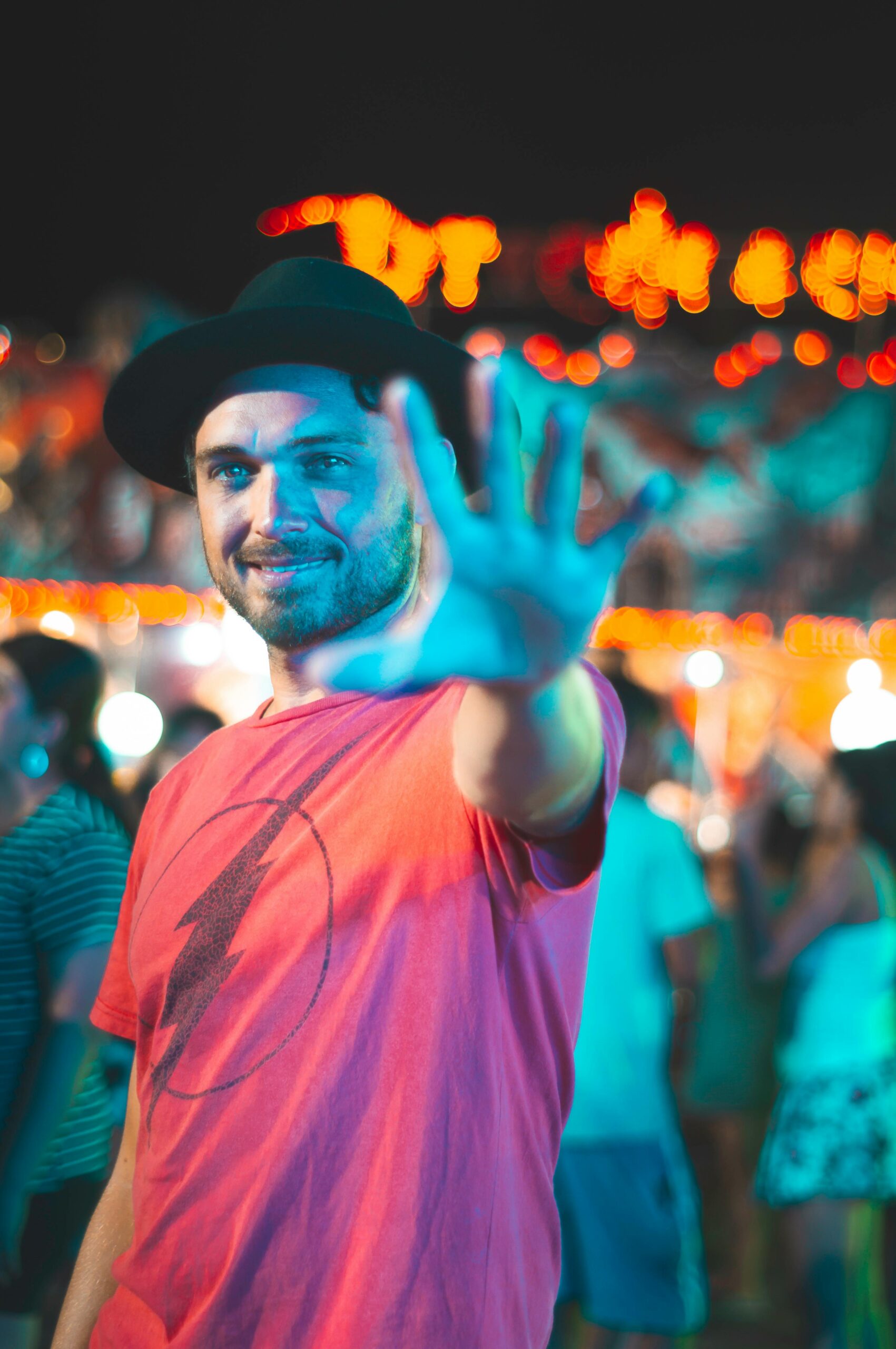 Man in a hat extending his hand towards the camera at a colorful night festival, ready to use his THCa cartridge from Wild Orchard.