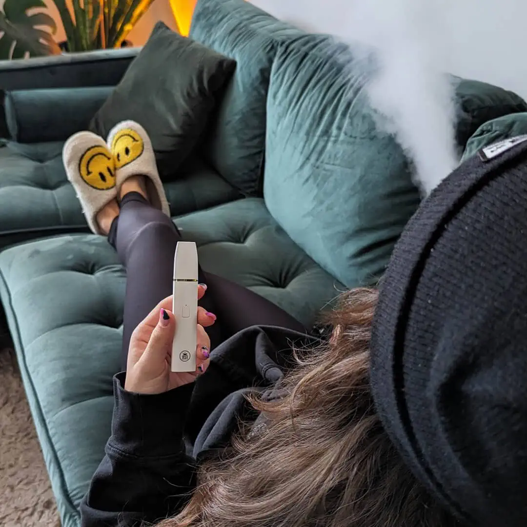A woman sitting on a couch with a vaporizer in her hand.