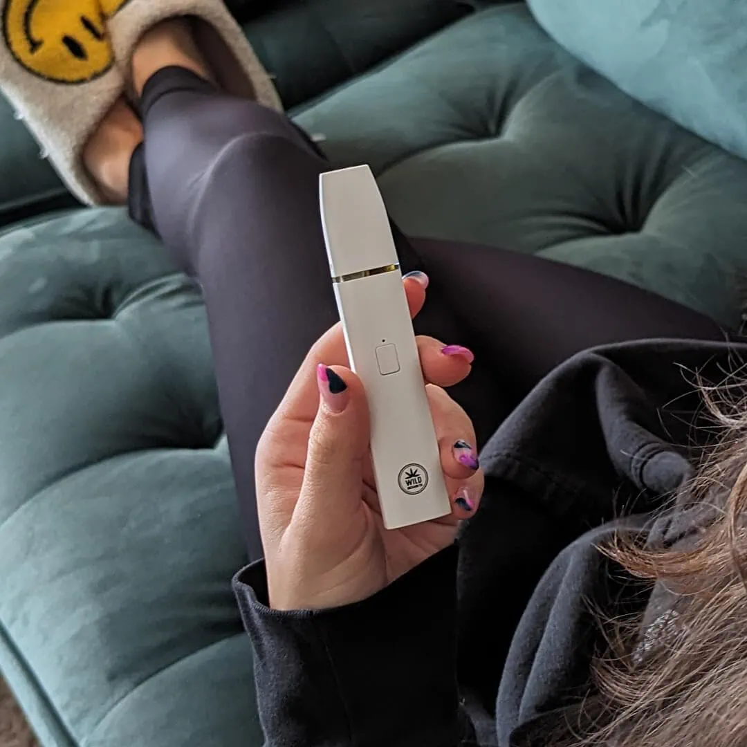 A woman sitting on a couch holding a vape pen.