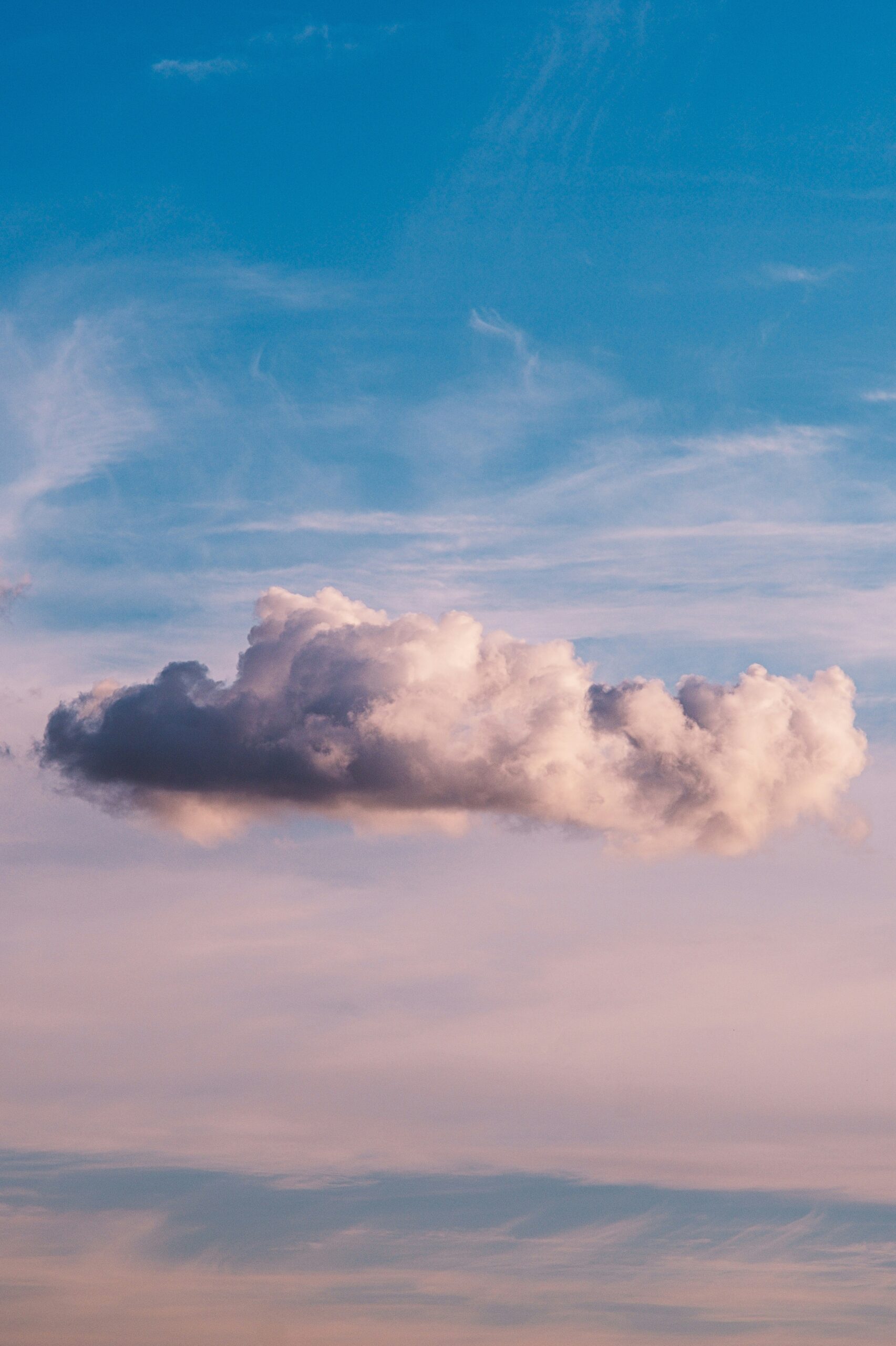 A solitary cumulus cloud against a pastel blue and pink sky at either sunrise or sunset.