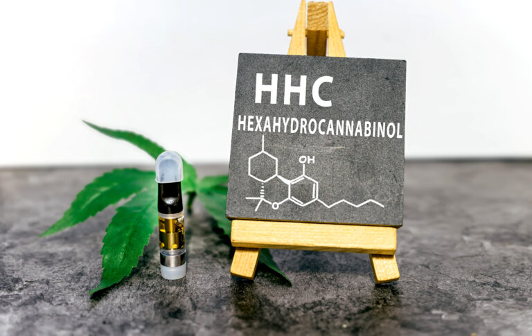 HHC chemical structure displayed on a mini chalkboard with a cannabis leaf and a vape cartridge in the background.