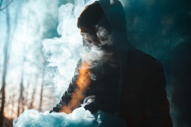 Person in a hoodie partially obscured by swirling smoke in a forest setting, with soft focus and a mystical ambiance, evoking questions like "What does HHC do for the body?